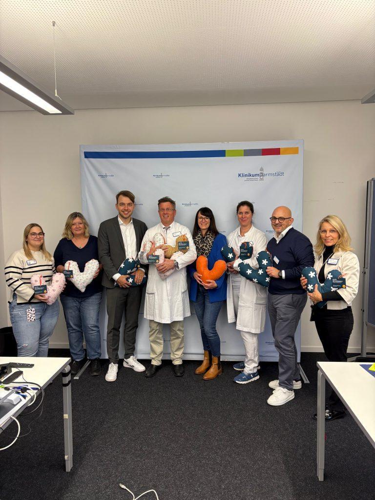 Gruppenfoto anlässlich der Übergabe der Herzkissen: (v.L.) Melanie Uhrig ( Krankenschwester auf der Station 11 D), Frau Brigitte Maurer (Breast Care Nurse ), Philipp Krämer (Leiter ENTEGA Unternehmenskommuniklation), PD. Dr. Sven Ackermann (Chefarzt/Klinikdirektor Frauenklinik), Julia Scheuch (ENTEGA), Katharina Rechel (leitende Oberärztin der Frauenklinik), Michelé Tarquinio ( pflegerischer Geschäftsführer ), Marion Rodehau (Hausdame) Foto: ENTEGA